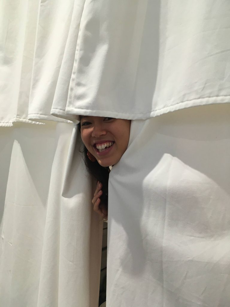 Photograph of Reina’s face peeking out from behind the ‘bathhouse’ curtains.