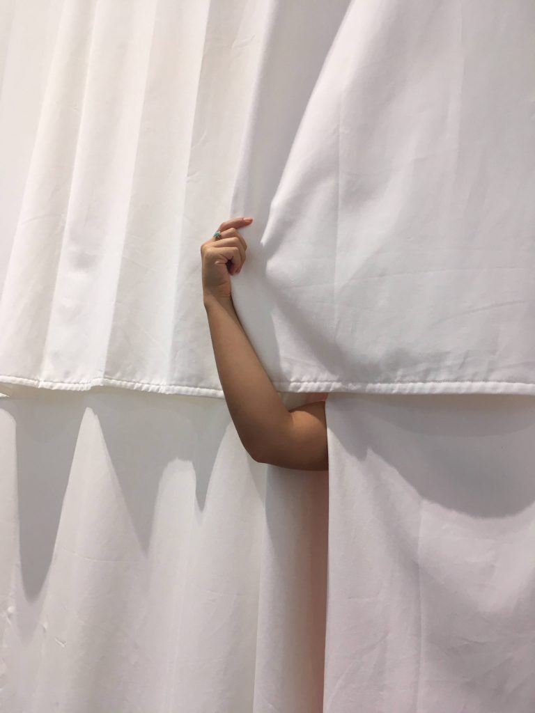 Photograph of Reina’s arm peeking out from the ‘bathhouse’ curtains.